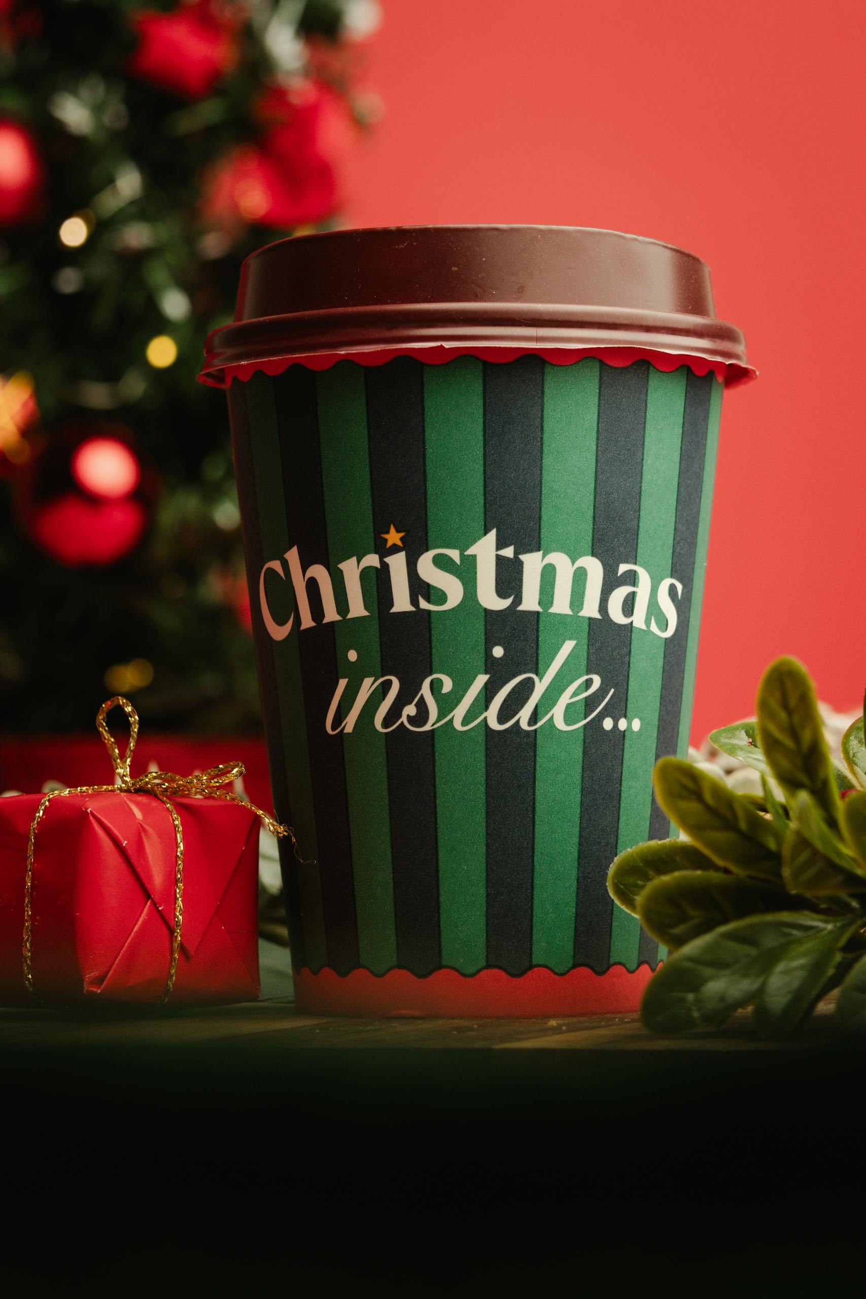 A vibrant Christmas-themed coffee cup surrounded by festive decor and plants, perfect for holiday promotions.